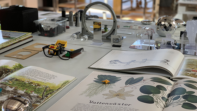 Ett bord med många prylar: Spegel, glasögon, lego, en bok.